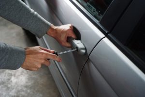 thief breaking into a car through the door
