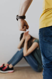 a man's fist hangs in front of the camera with a woman against a wall trying to prevent being hit